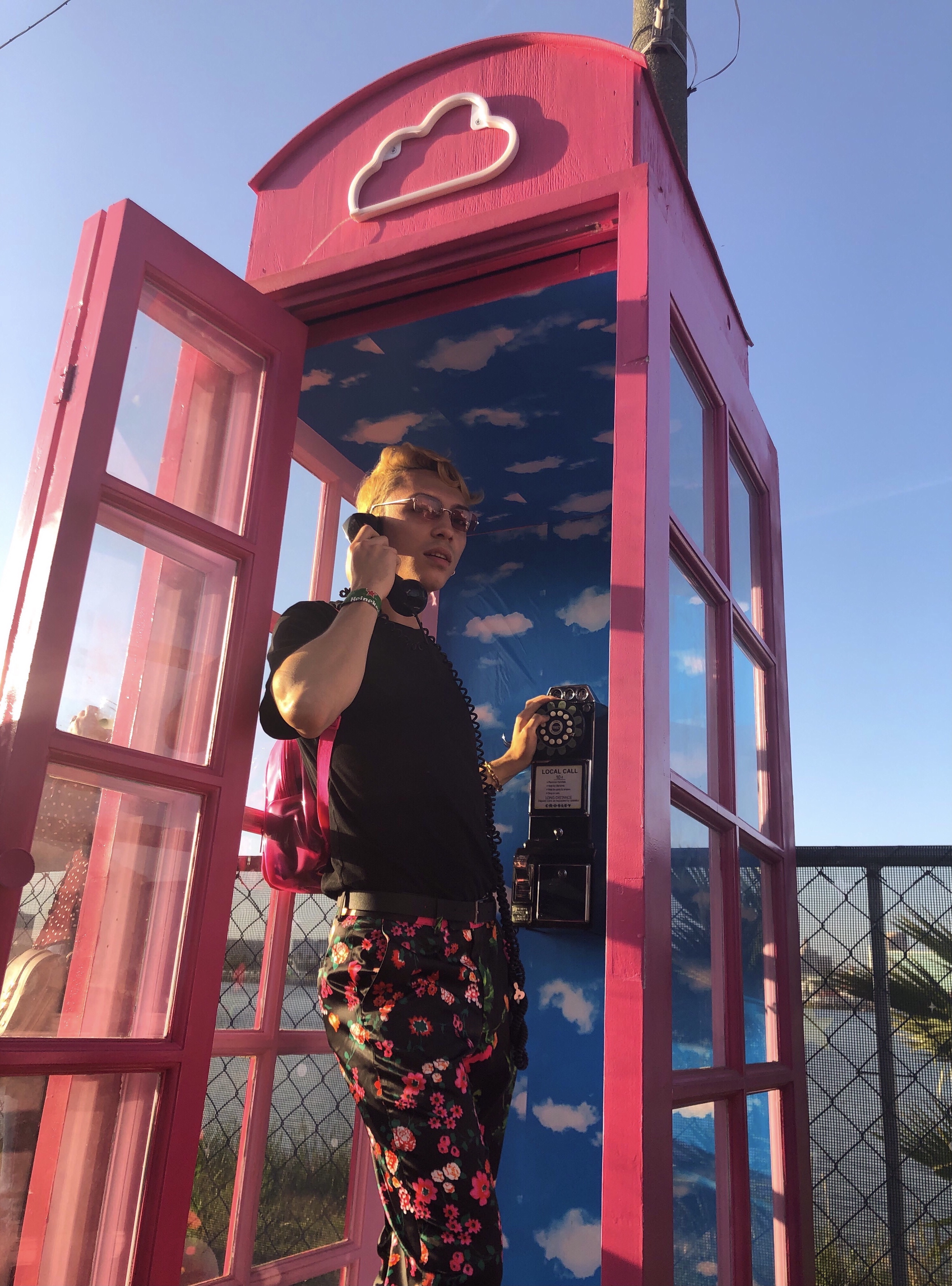 Stephen wearing flower print pants while standing in a phone booth